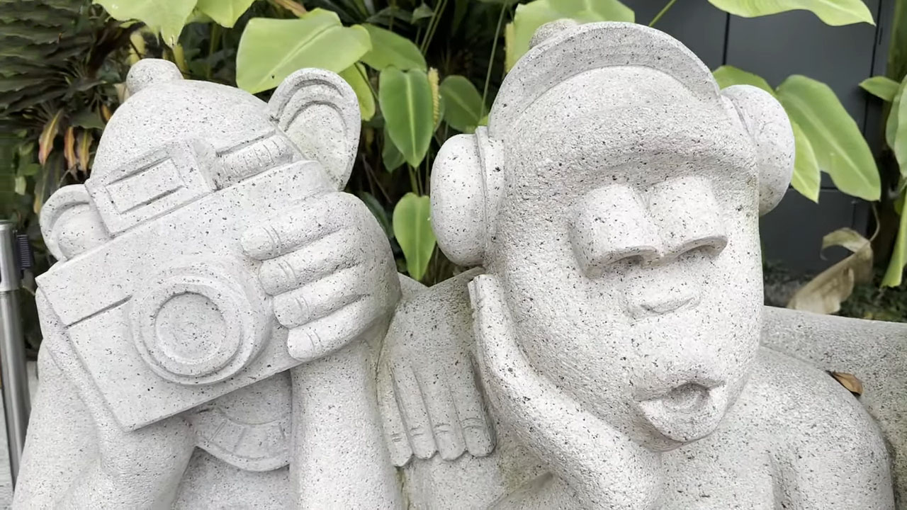 Stone sculpture of two monkeys in the Children's Garden, one holding a camera and the other wearing headphones